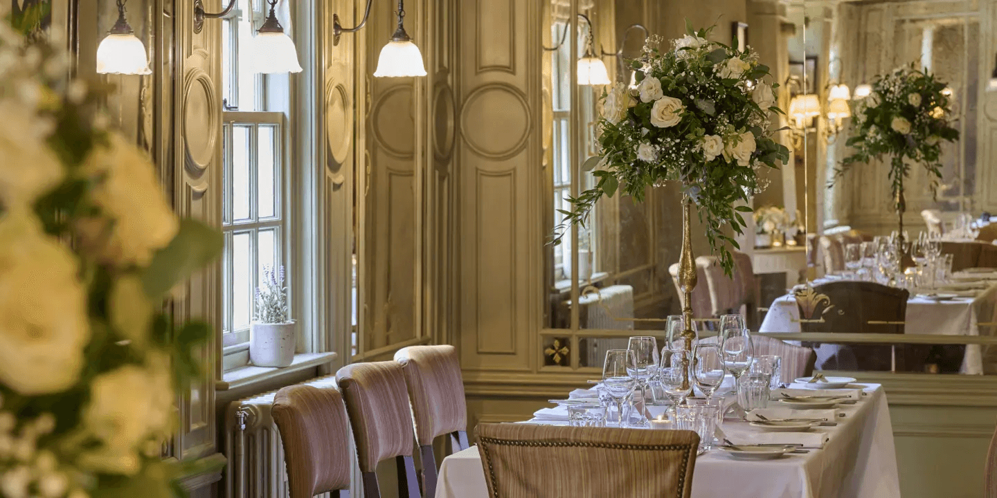 Elegant private dining room with tall floral centrepiece, white linen and panelled walls.