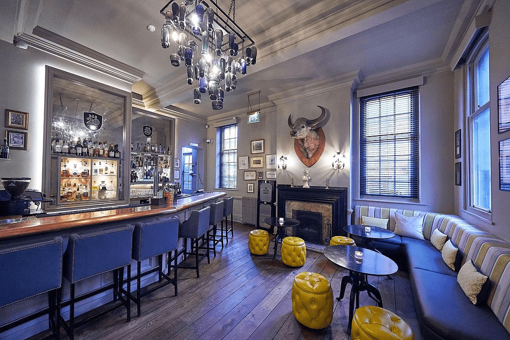 The bar area at Hotel du Vin Winchester with yellow ottomans and a bull's head mount.