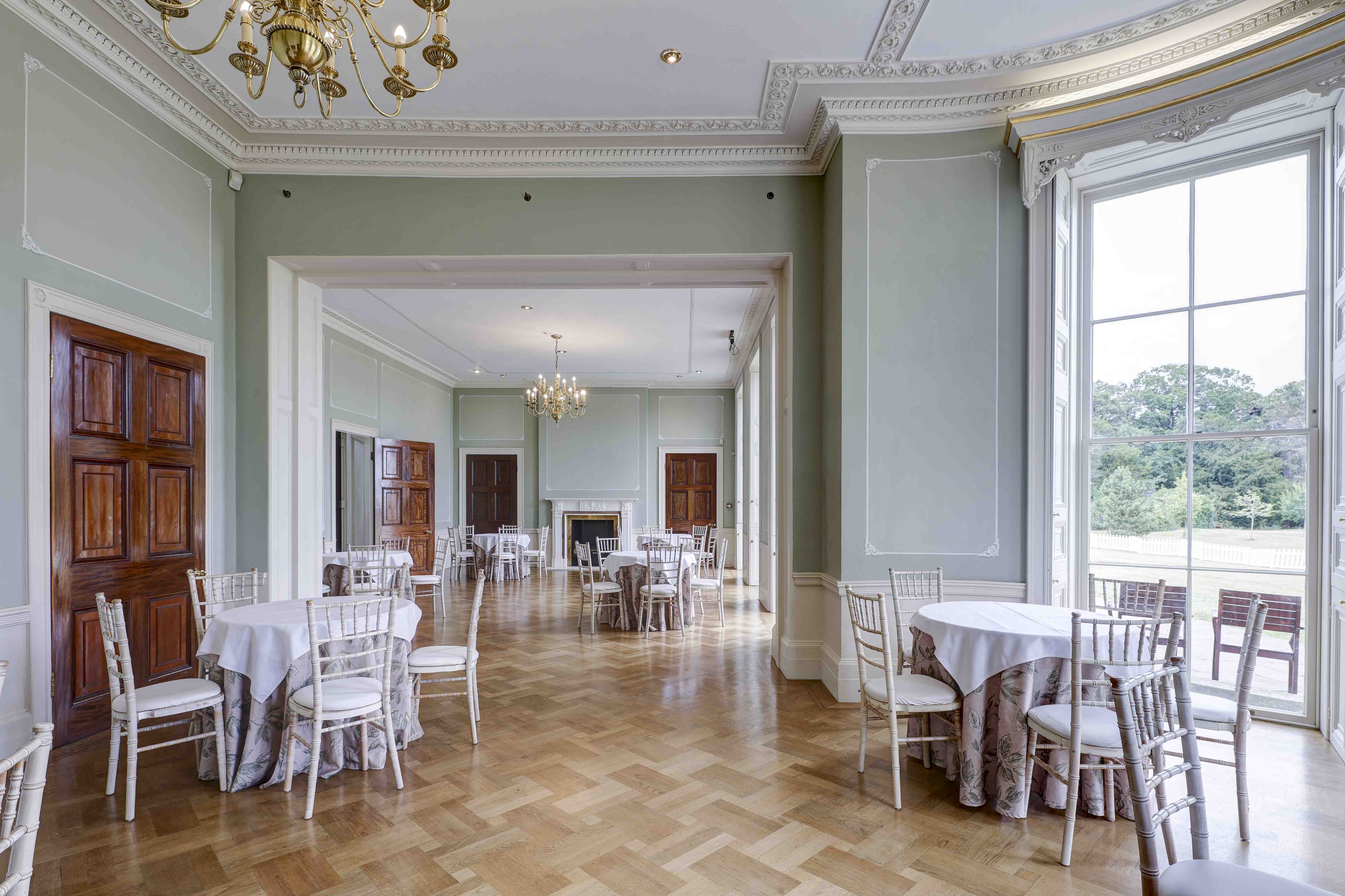Elegant function room at Hylands Estate with parquet flooring, chandeliers and round tables.