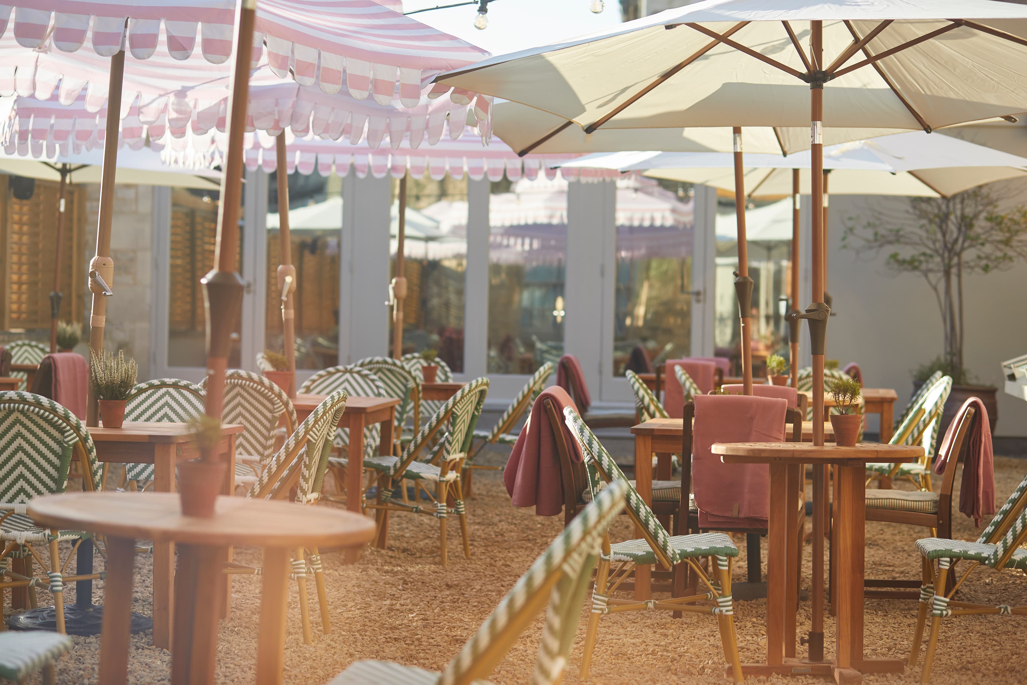 Outdoor terrace with rattan bistro chairs, wooden tables and pink striped parasols.