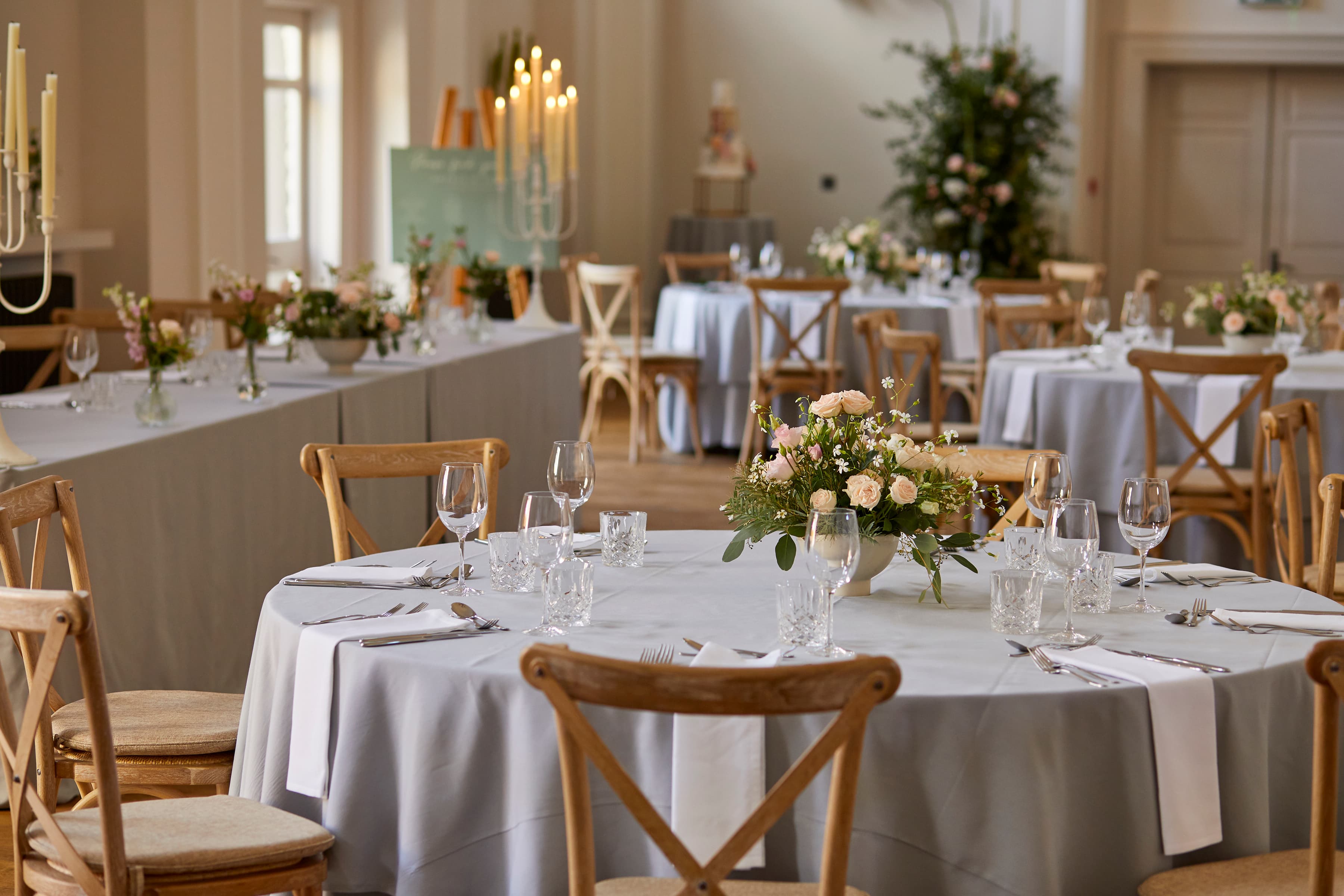 Wedding reception room with round tables, cross-back chairs and floral centrepieces at Kings Head Cirencester.