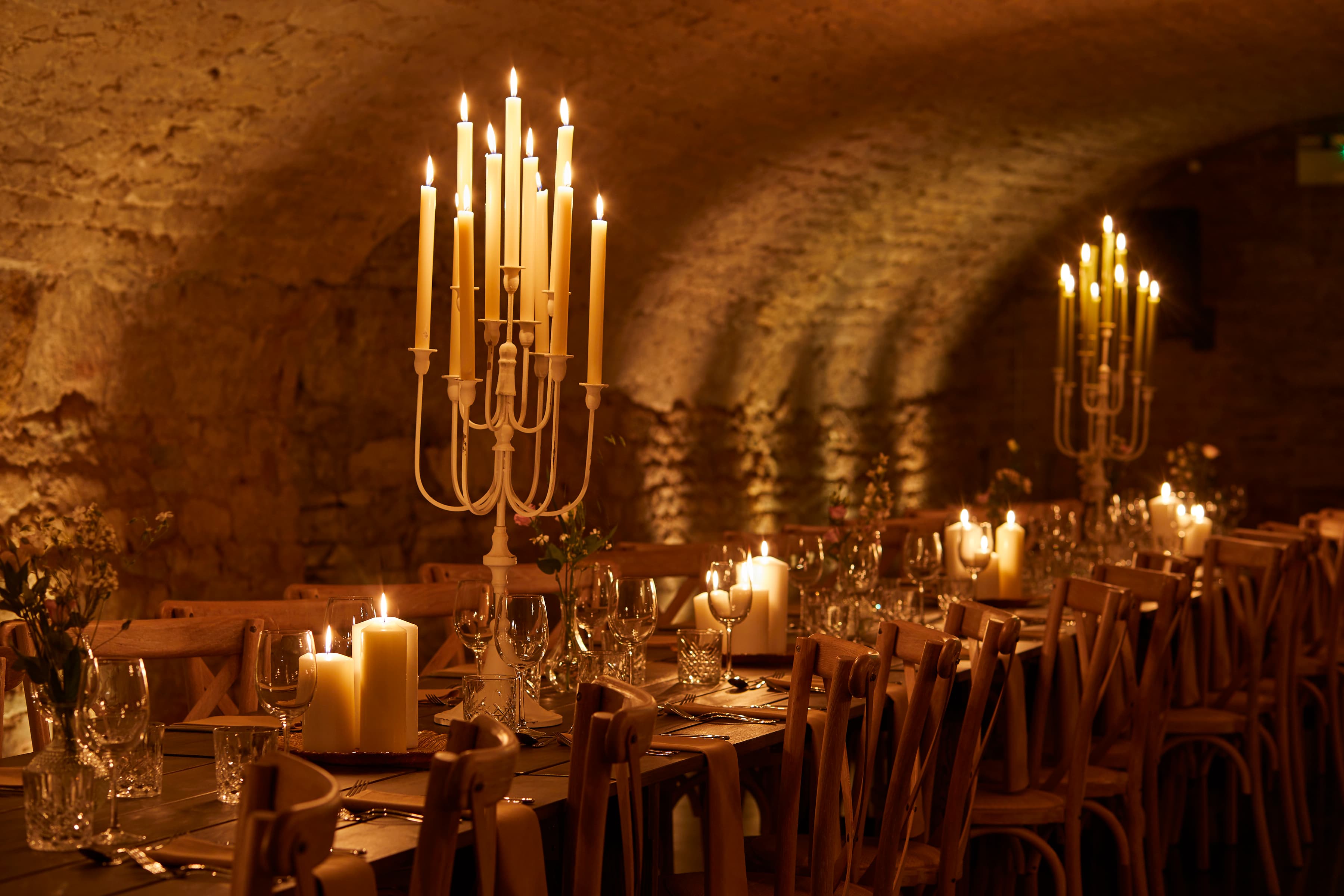 Stone vaulted cellar dining room set with candelabras, pillar candles and glassware.