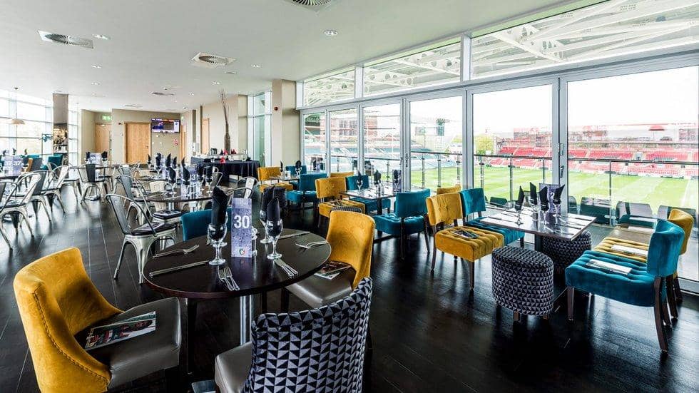 Hospitality dining room with teal and gold chairs overlooking the rugby pitch at Welford Road.