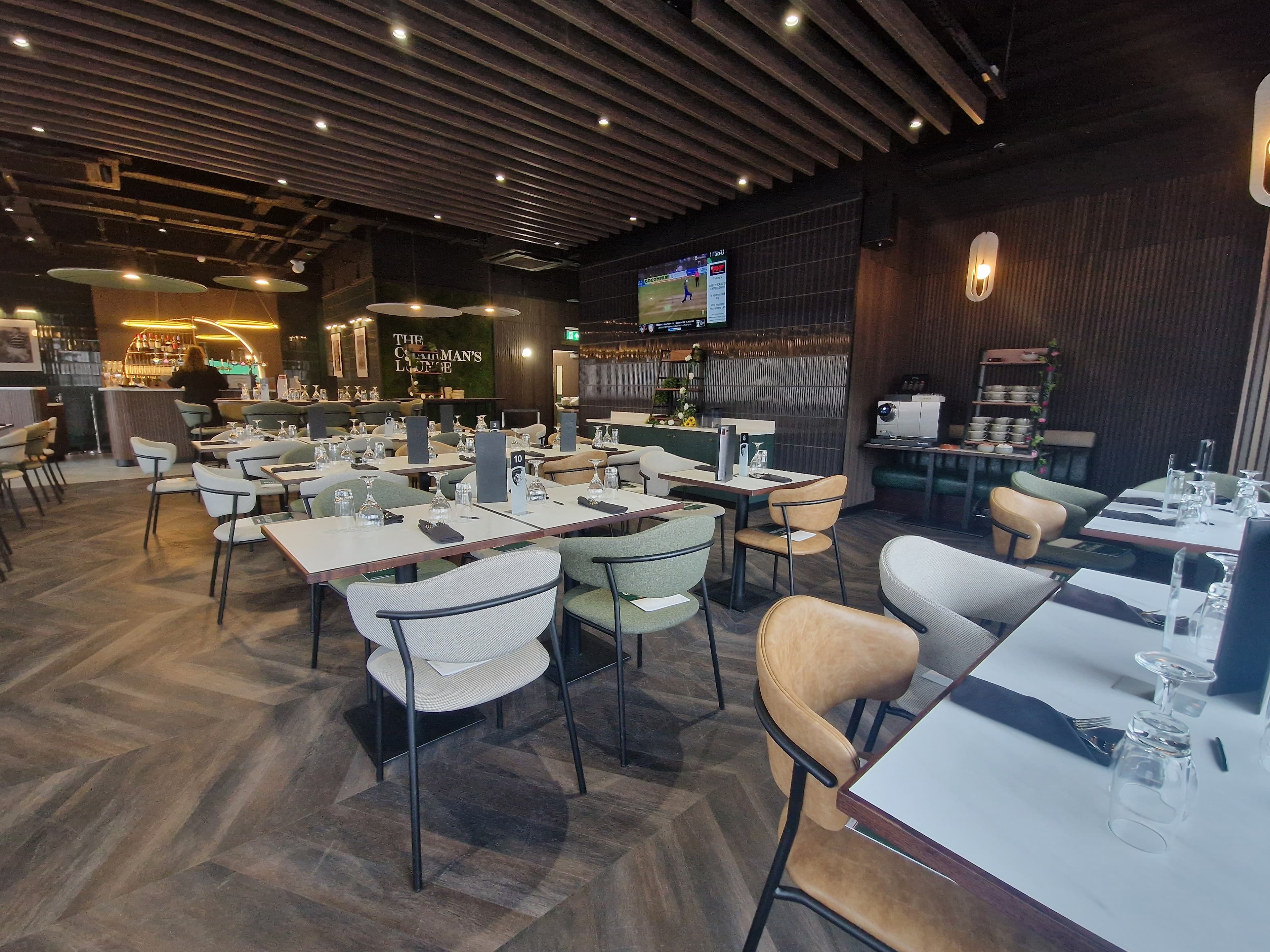 The Chairman's Lounge dining room with laid tables, mixed upholstered chairs and a bar area.
