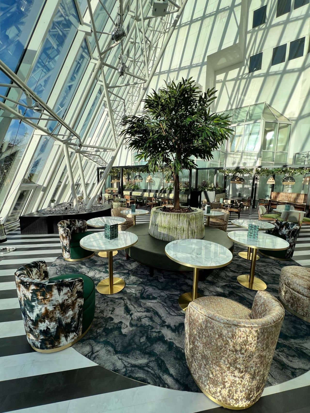 Bright hotel atrium bar with marble tables, velvet chairs and a large indoor tree.