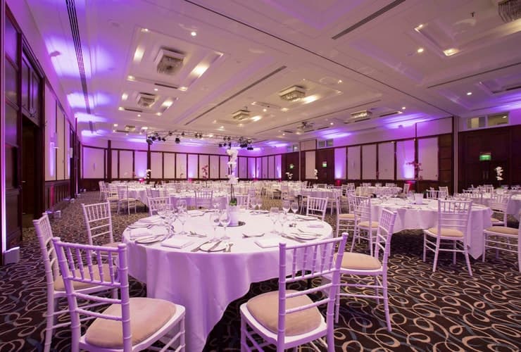 Ballroom set for a banquet with round tables, white chiavari chairs and purple uplighting.