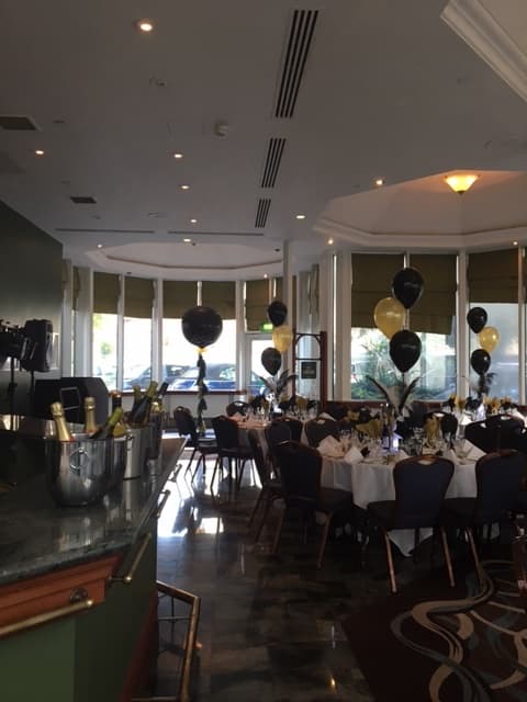 Function room set for a celebration with black and gold balloons and round tables.