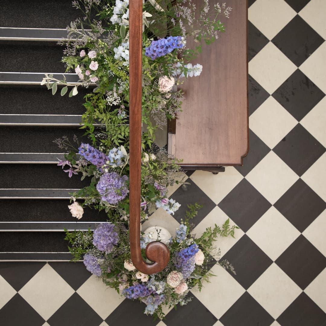 Overhead view of a staircase handrail dressed with blue, lilac and pink flowers.