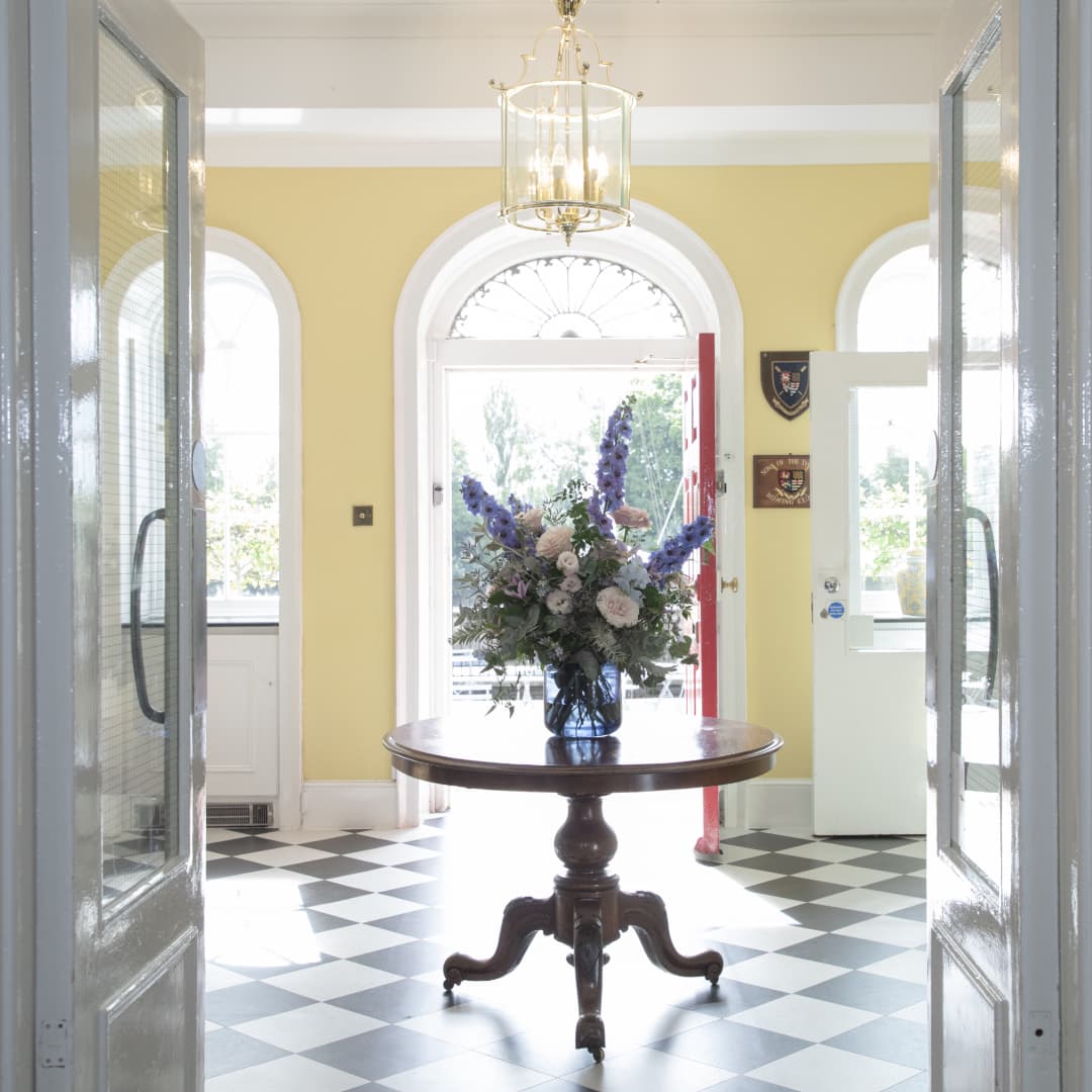 Entrance hall with black and white tiled floor, round wooden table and floral arrangement.