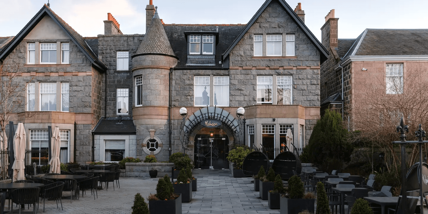 Exterior of Malmaison Aberdeen showing a granite façade, arched entrance and outdoor terrace seating.