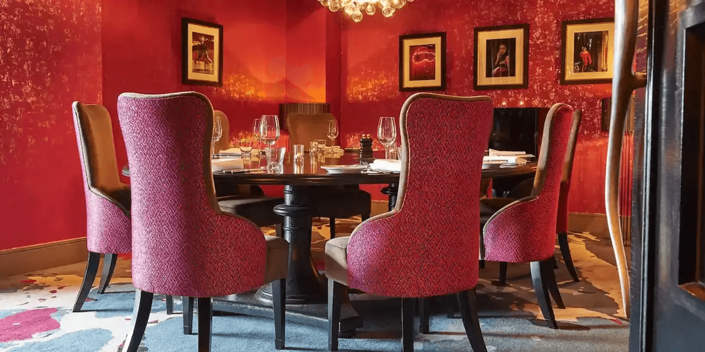 Private dining room with a round table, red walls and upholstered chairs at Malmaison Aberdeen.