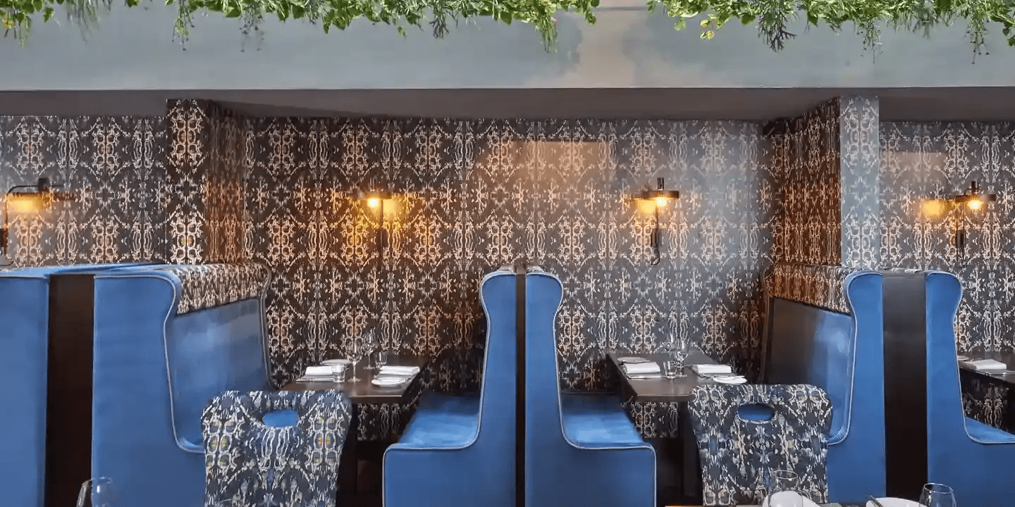 Plush blue booth seating and patterned wallpaper in a restaurant dining area.