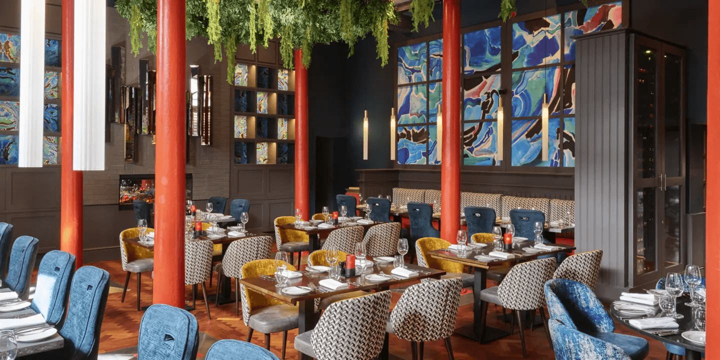 Restaurant dining room with red columns, colourful artwork and mixed velvet seating at Malmaison Belfast.