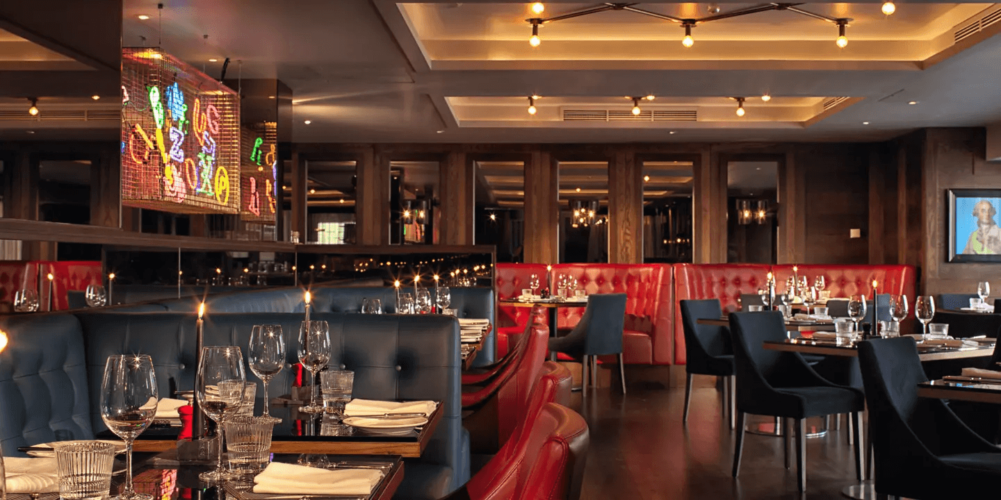 Dimly lit restaurant interior with red and blue leather booths and laid tables