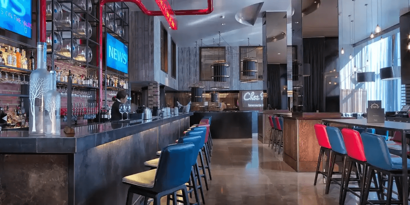 The bar interior at Malmaison Birmingham with blue and red bar stools and neon signage.