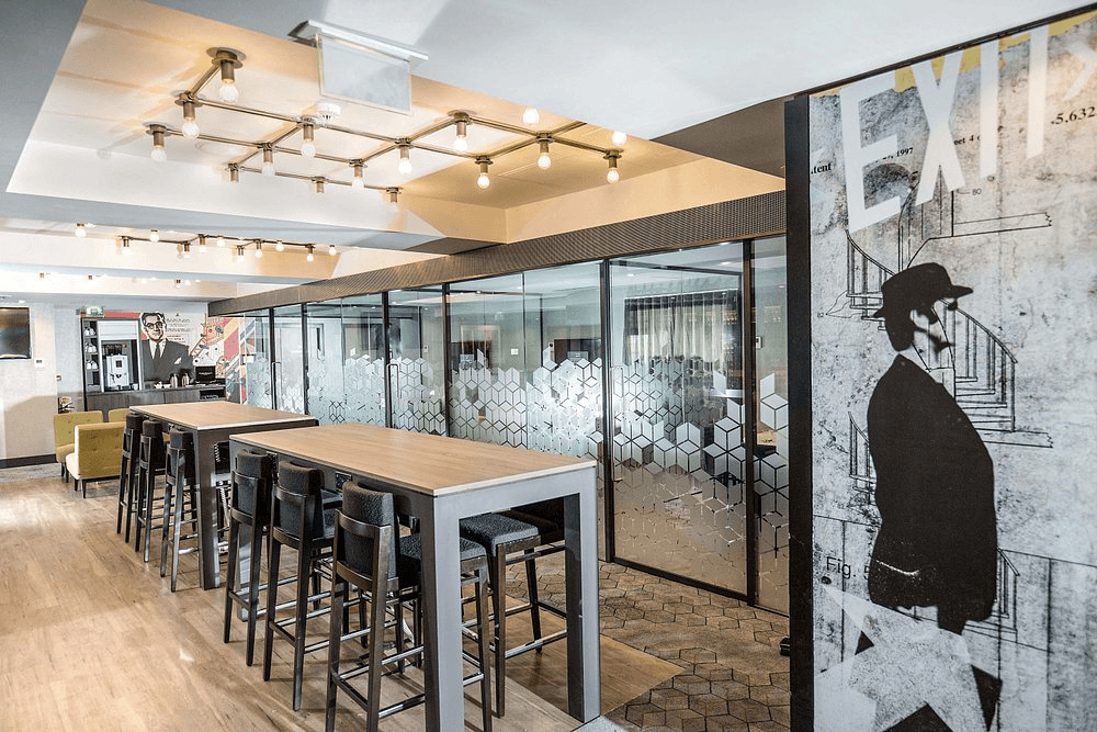 Bar area with high tables, stools and a glass-partitioned private dining room beyond.