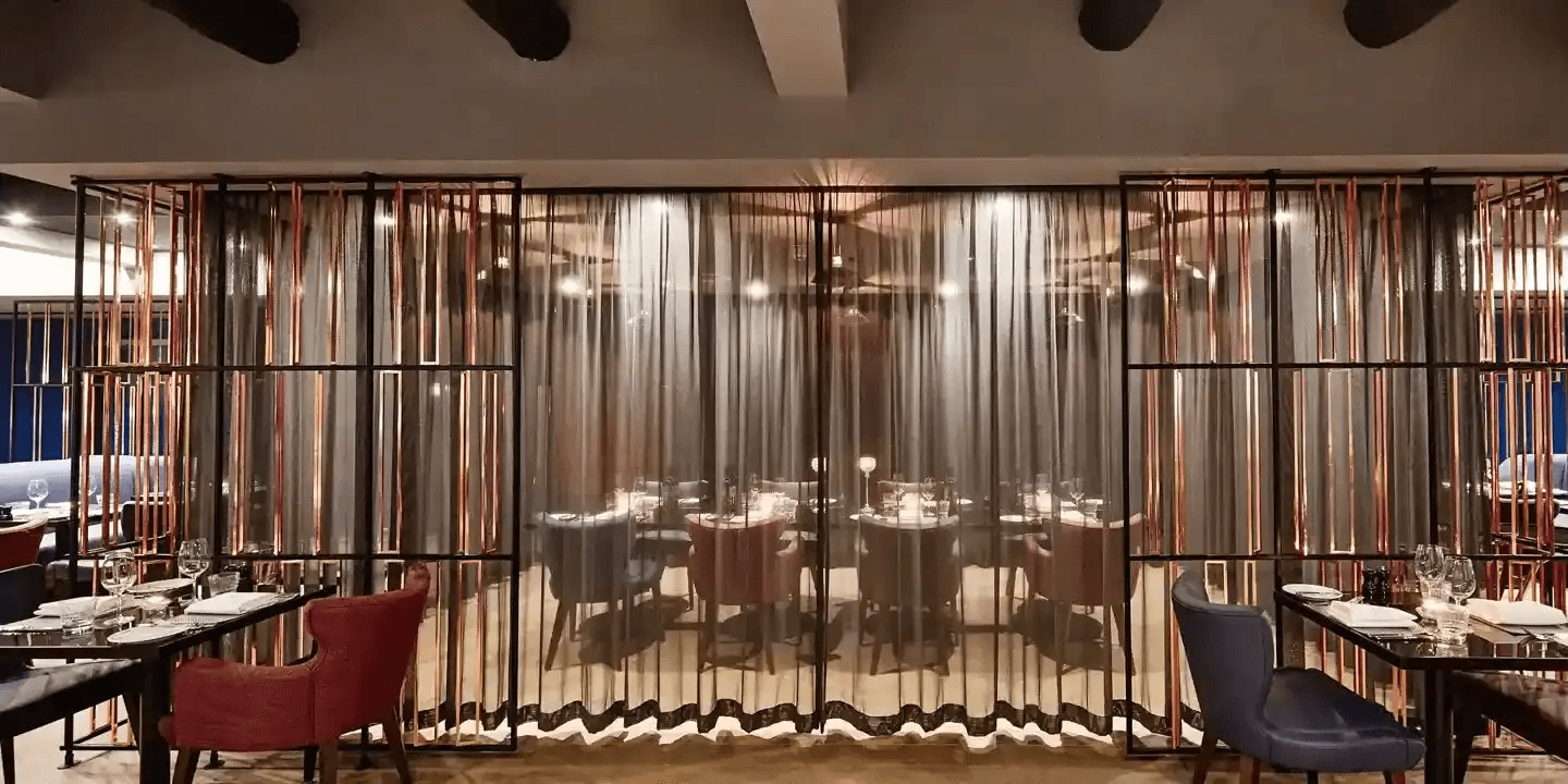 Dimly lit restaurant dining area with copper screen dividers and upholstered chairs
