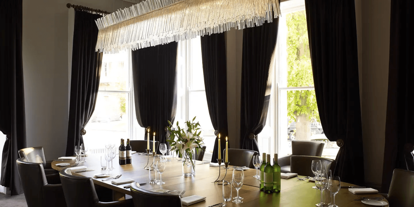 Private dining room at Malmaison Cheltenham with a long laid table and crystal chandelier.