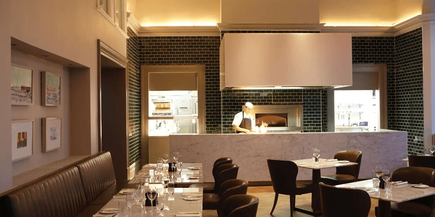 Restaurant dining room with open kitchen, marble counter and dark green tiled walls.