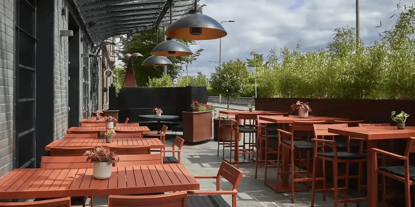 Outdoor terrace at Malmaison Dundee with red wooden tables, bar stools and overhead heaters.