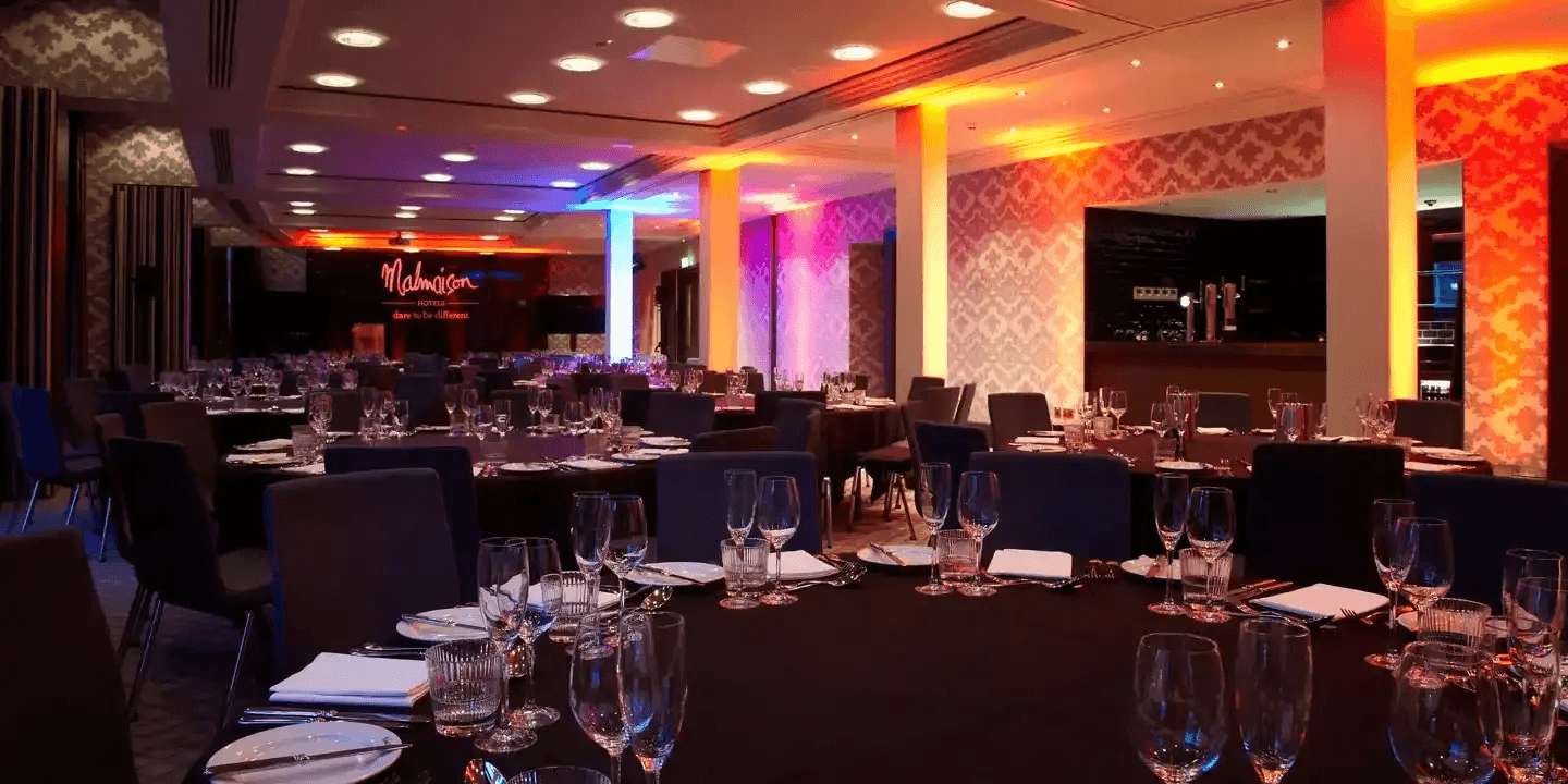 Malmaison Dundee event room laid for a dinner with colourful uplighting and round tables.