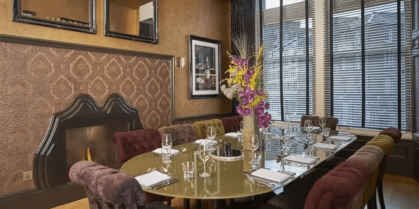 Private dining room with a lit fireplace, velvet chairs and a laid table.