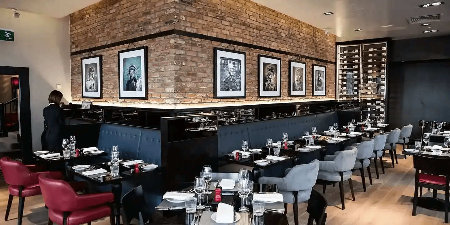 Restaurant dining room with exposed brick walls, framed artwork and laid tables.