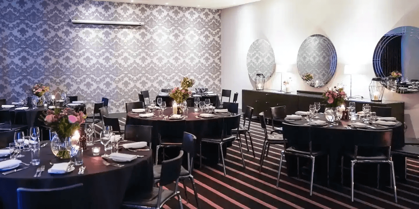 Private dining room with round tables, floral centrepieces and damask wallpaper at Malmaison Edinburgh.