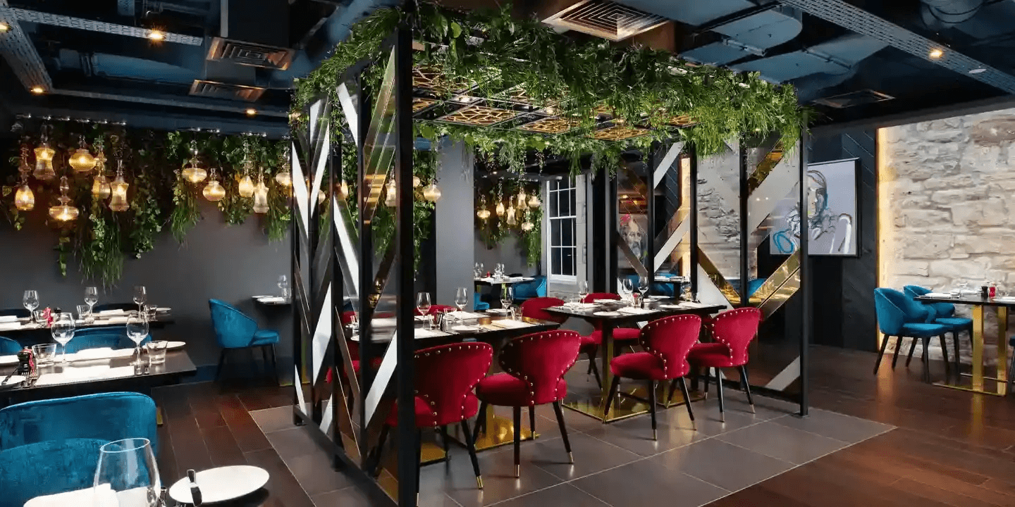 Restaurant interior with red velvet chairs, trailing greenery overhead and globe pendant lights.