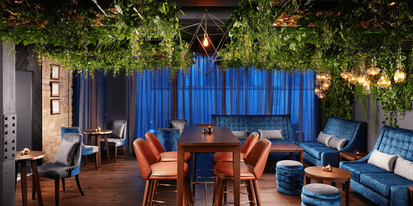 Cocktail bar with lush ceiling greenery, blue velvet sofas and leather bar stools.