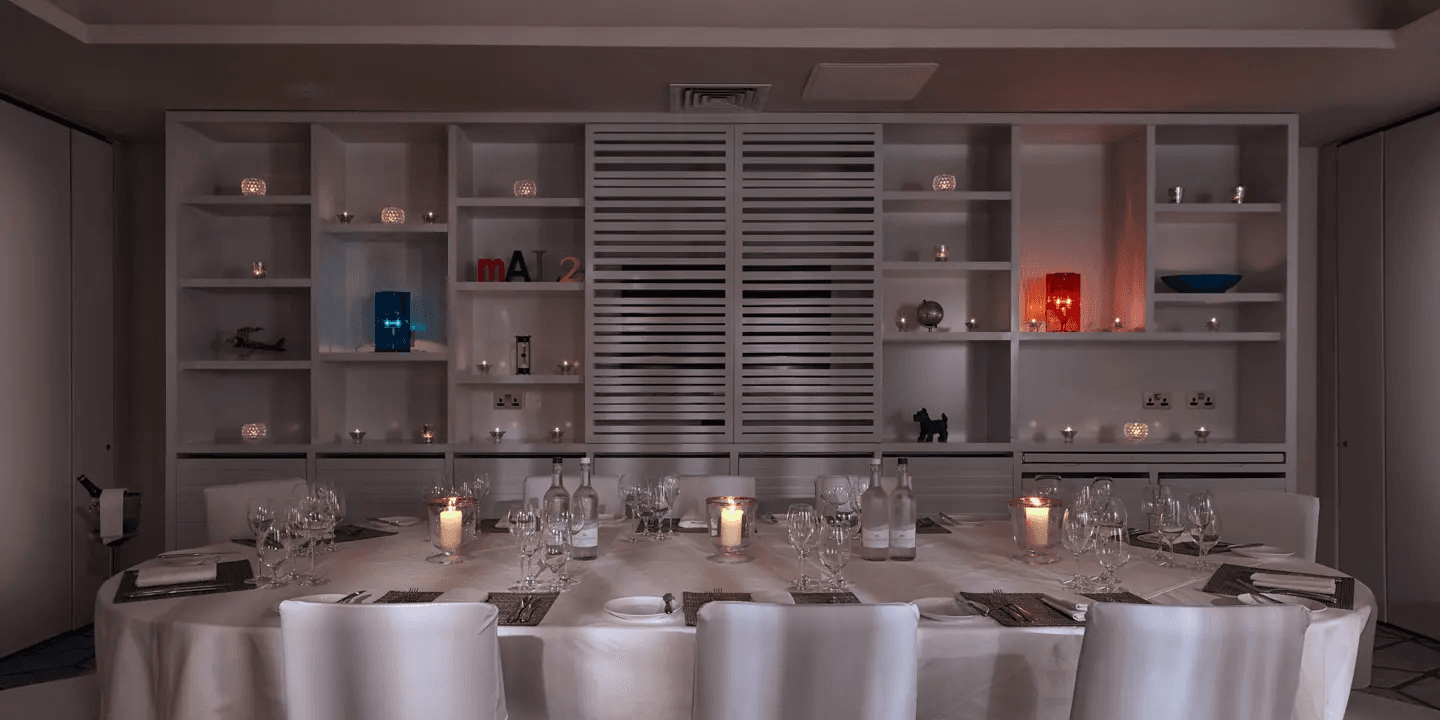 Private dining room with oval table, white chairs and candlelit shelving unit behind.