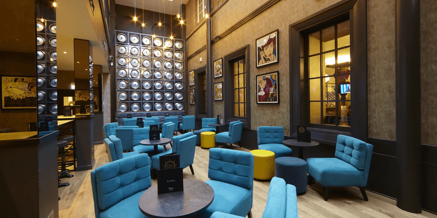 Stylish hotel bar with teal armchairs, yellow stools and pop art wall prints.