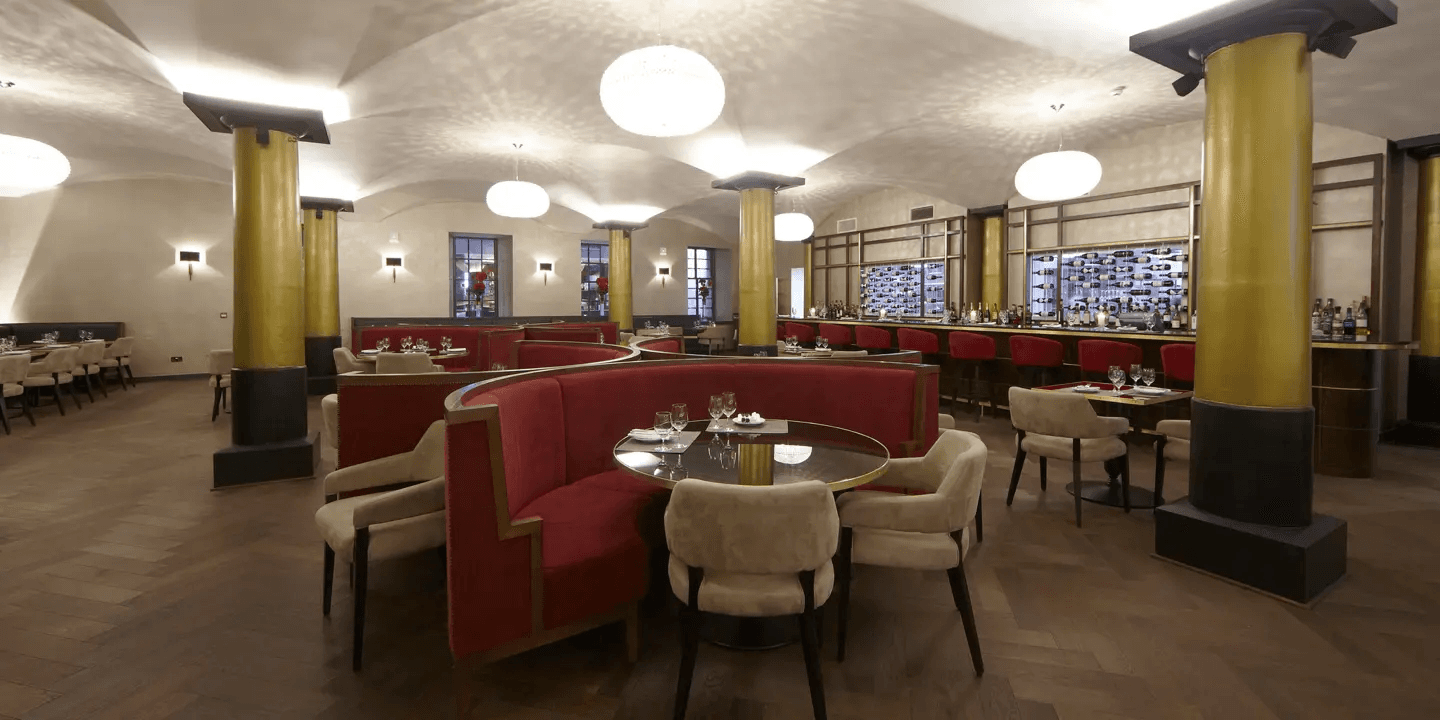 Restaurant interior with red curved booths, gold columns and a bar backdrop.