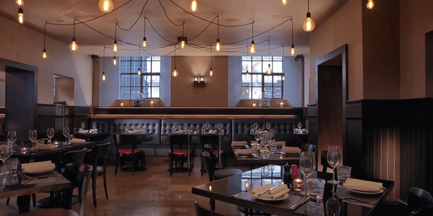 Dimly lit restaurant dining room with Edison bulb ceiling lights and leather banquette seating