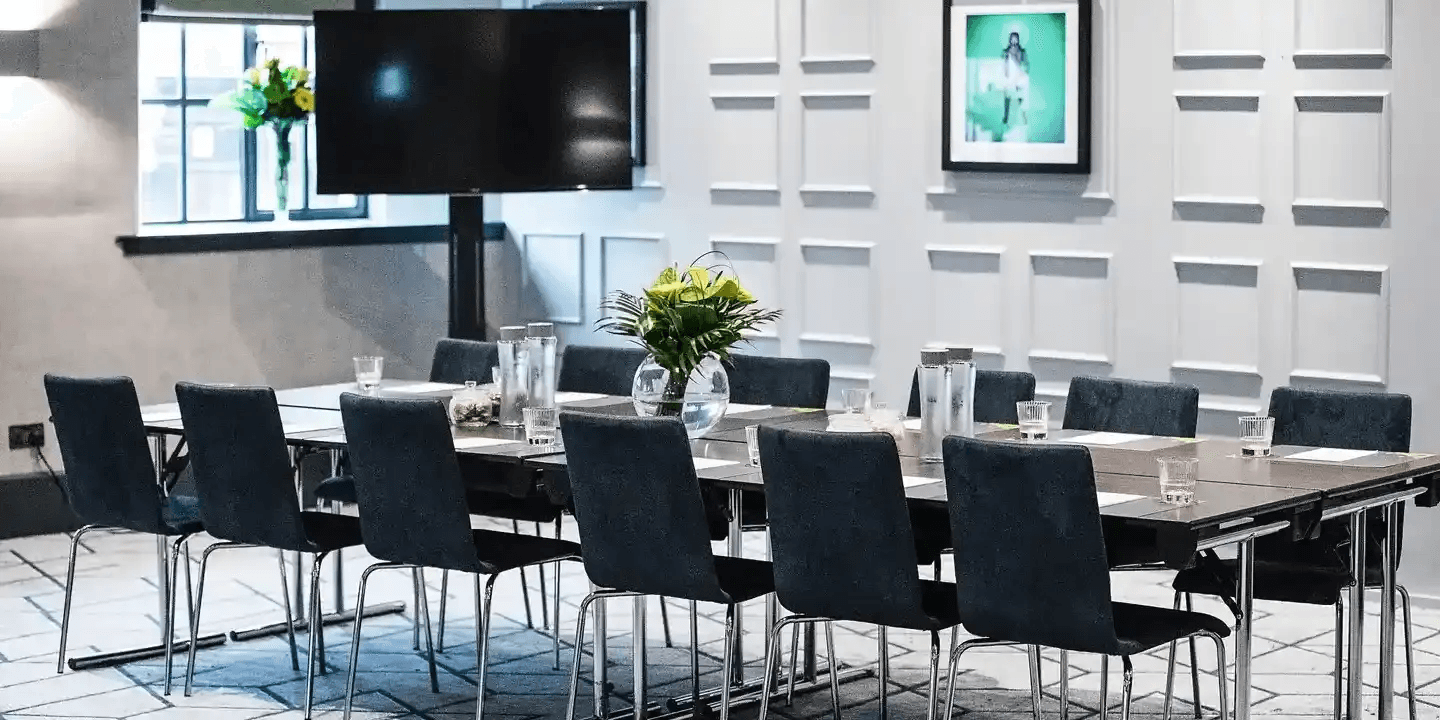 Meeting room at Malmaison Leeds set with tables, chairs, water and a wall-mounted screen.