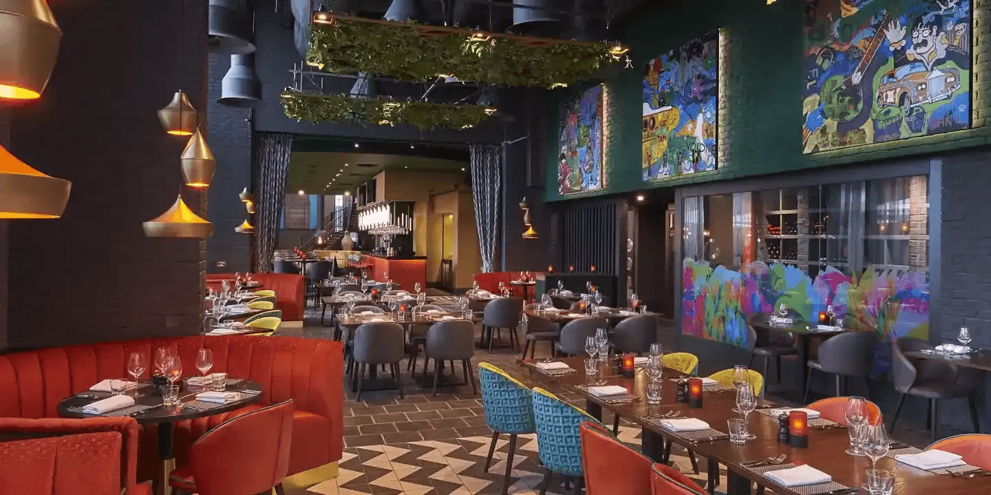 Dimly lit restaurant dining room with colourful artwork, mixed seating and trailing ceiling greenery.