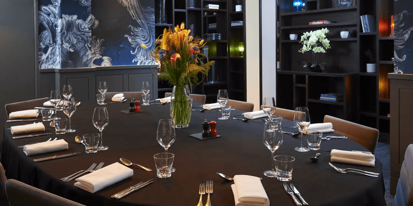 Private dining room at Malmaison London with a laid round table and floral centrepiece.