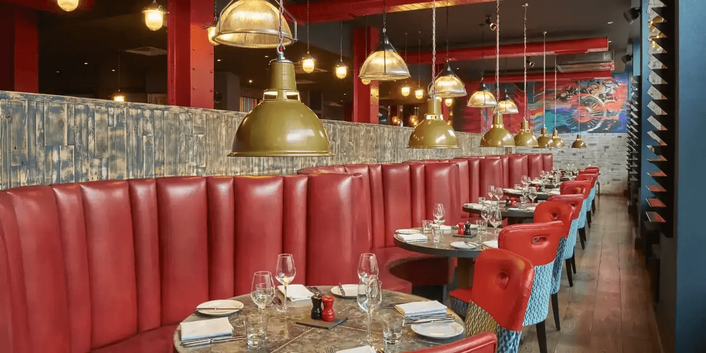 Red leather banquette seating and brass pendant lights in a restaurant dining room.