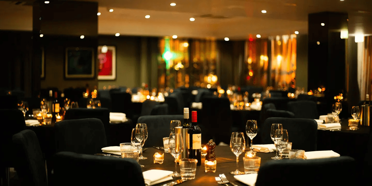 Candlelit dining room at Malmaison Manchester with dark chairs and wine on tables.