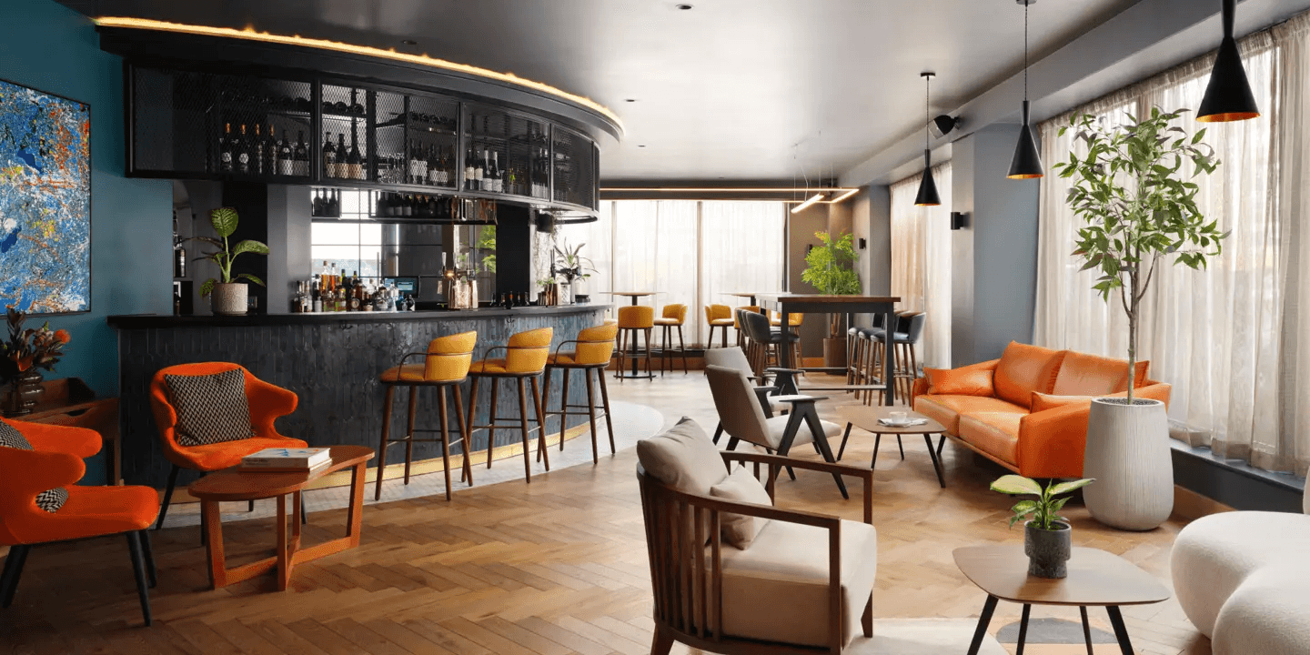 Stylish hotel bar lounge with orange seating, yellow bar stools and parquet flooring.