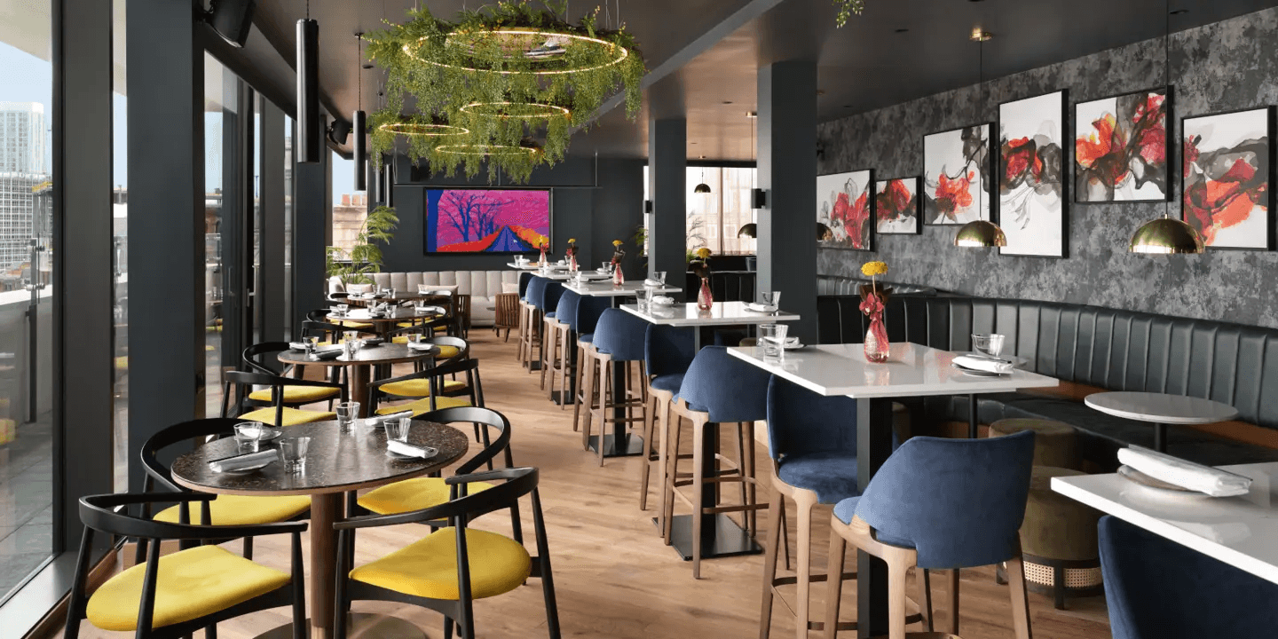 Bright restaurant interior with yellow chairs, blue bar stools, banquette seating and bold artwork.
