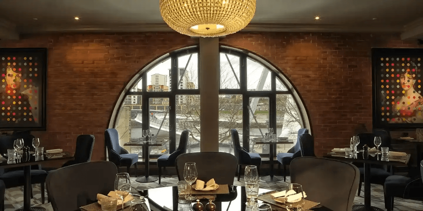 Restaurant interior with arched window overlooking the River Tyne and colourful pop art portraits.