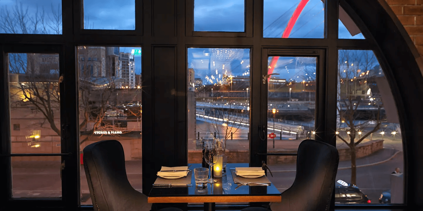 Window table for two with candlelight and views over the Gateshead Millennium Bridge at dusk.