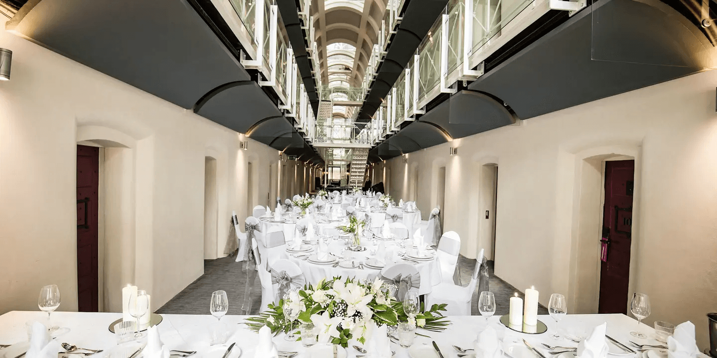 Former prison wing set for a formal dinner with round tables and white floral centrepieces.