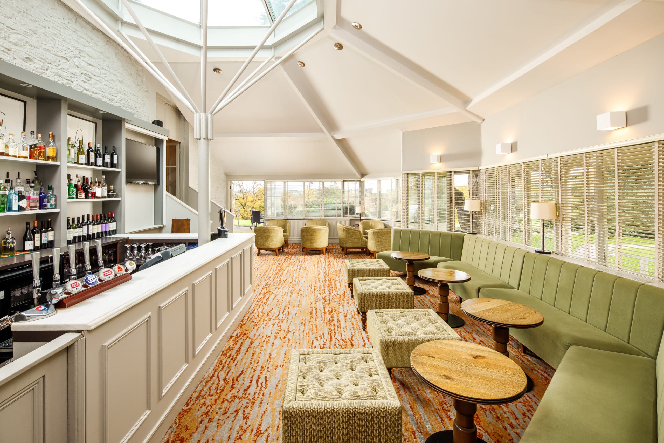 Bright hotel bar and lounge with green banquette seating and patterned carpet.