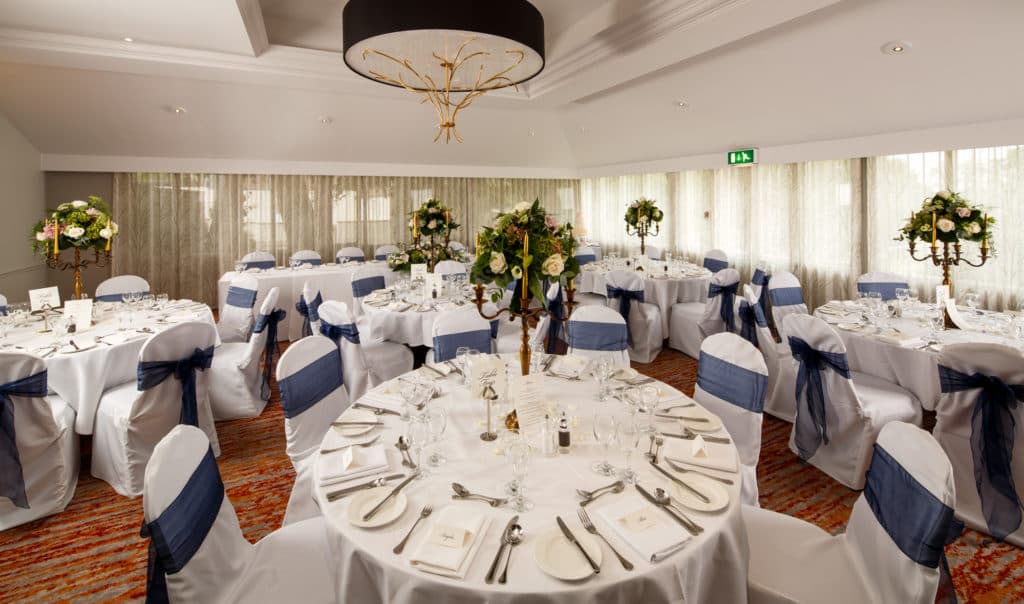 Banqueting room with round tables, white chair covers and navy sashes at Mercure Bristol North The Grange Hotel.