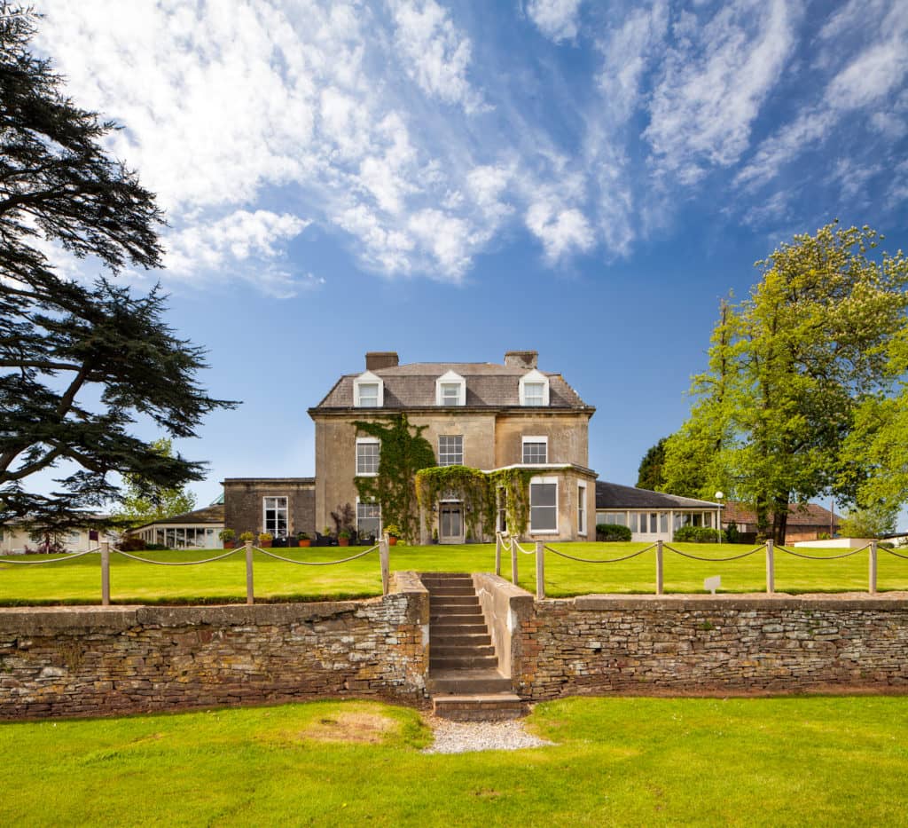 Stone manor house exterior with ivy-clad facade, manicured lawns and dry stone wall.