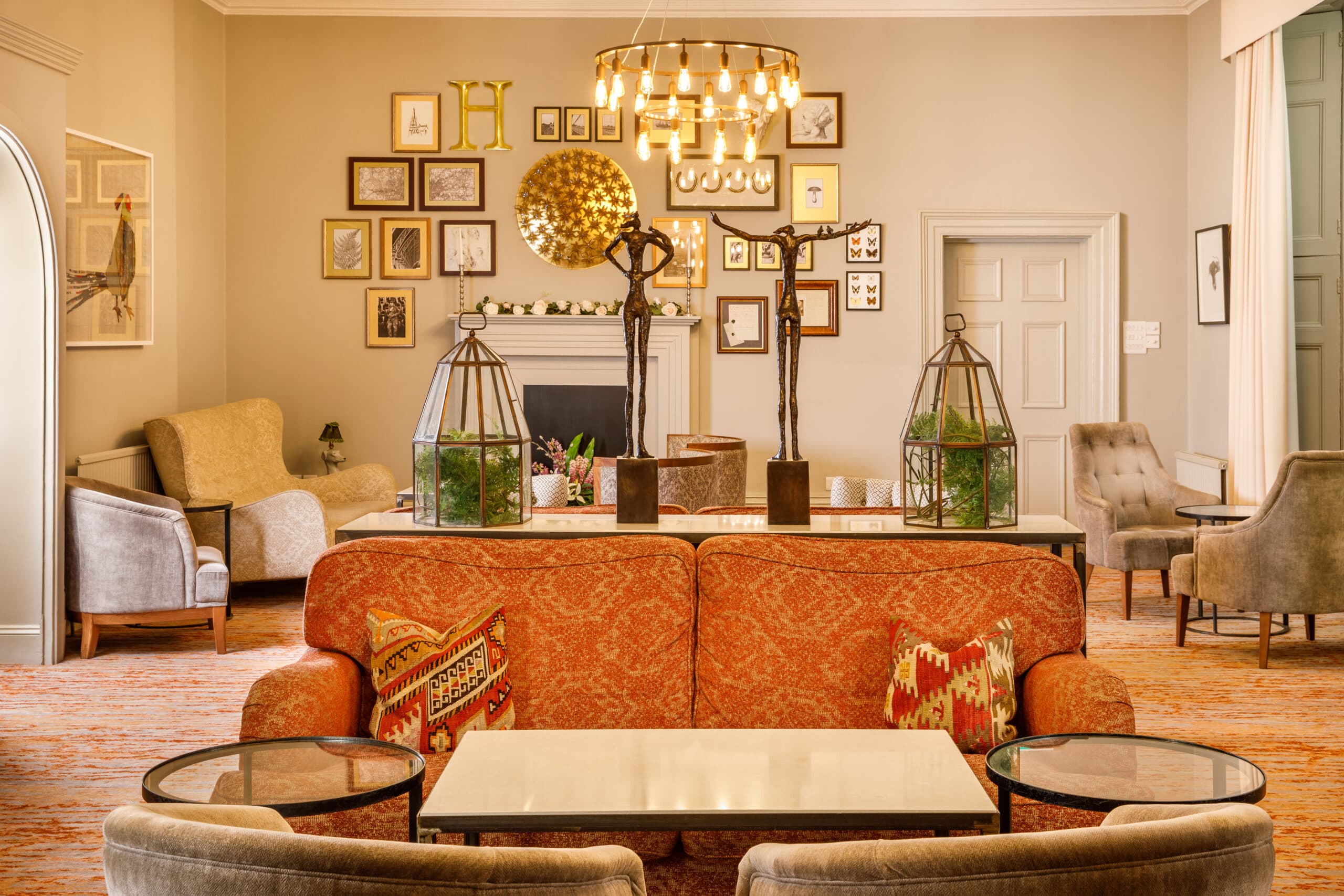 Hotel lounge with orange sofa, gallery wall, bronze sculptures and glass terrariums.