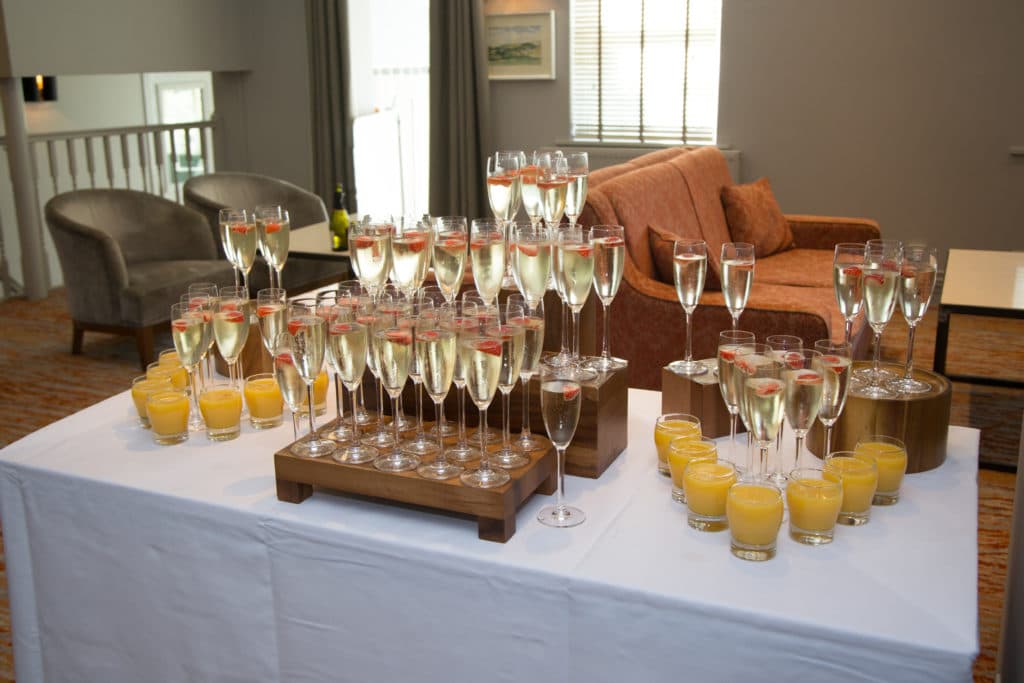 Champagne flutes with strawberries and glasses of orange juice on a white-clothed table