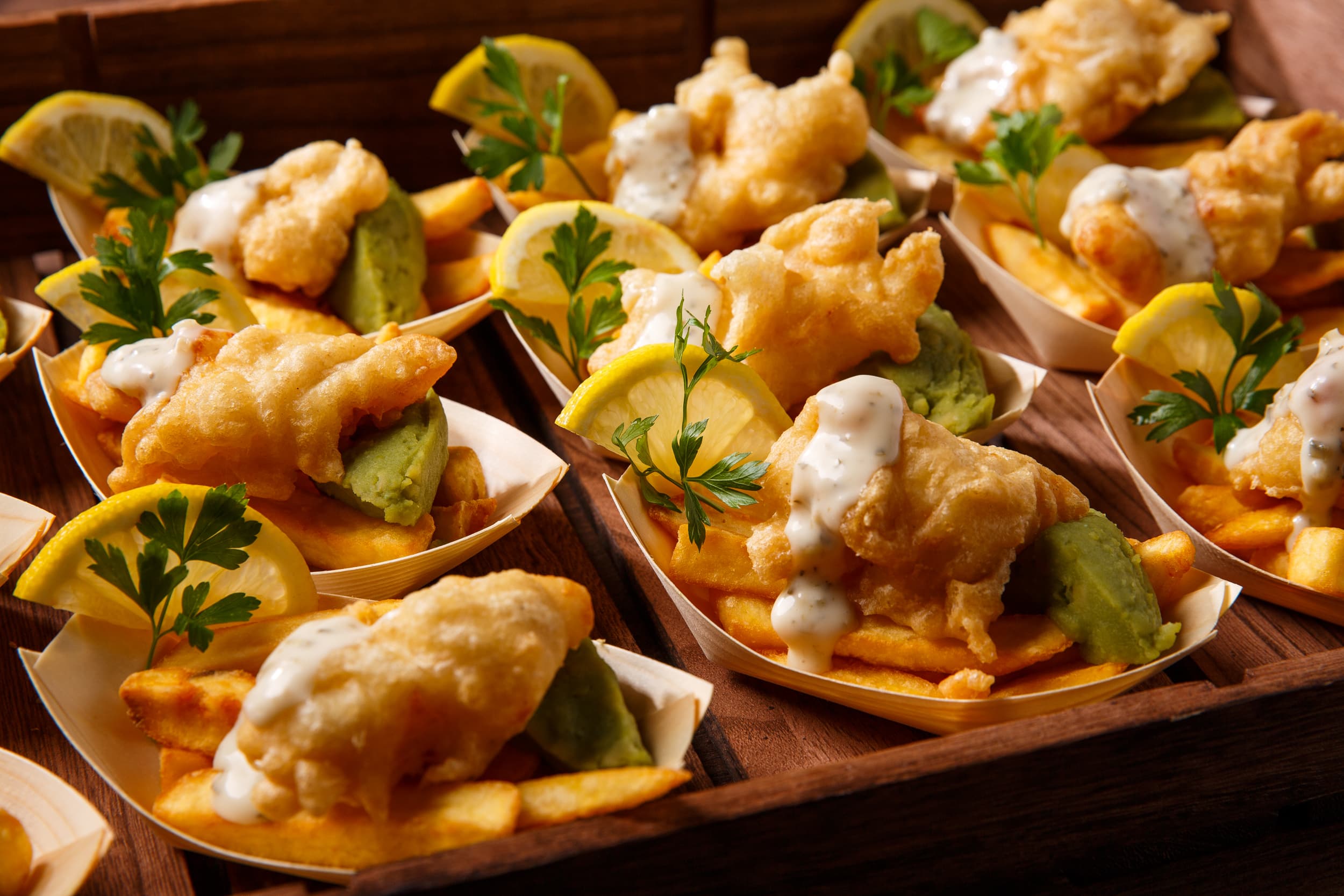 Individual portions of battered fish and chips with tartare sauce, mushy peas and lemon wedges.